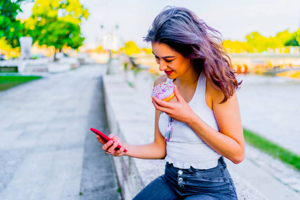 istock Smiling woman texting and eating donut 1317673454