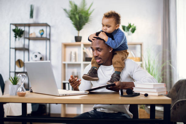 istock Busy afro man working on laptop with son on neck 1317675634