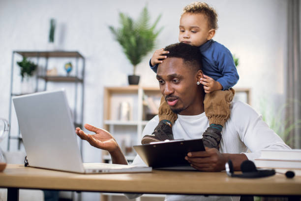 istock Busy afro man working on laptop with son on neck 1317675642