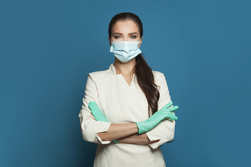 Happy doctor or nurse woman in protective medical mask and surgical gloves on blue background.  Medicine, assistance, safety and virus covid-19 protection concept
