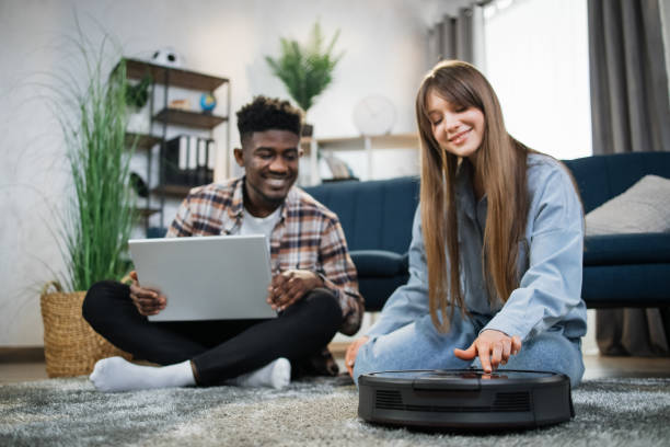 istock Young diverse couple using robot vacuum cleaner at home 1317678447