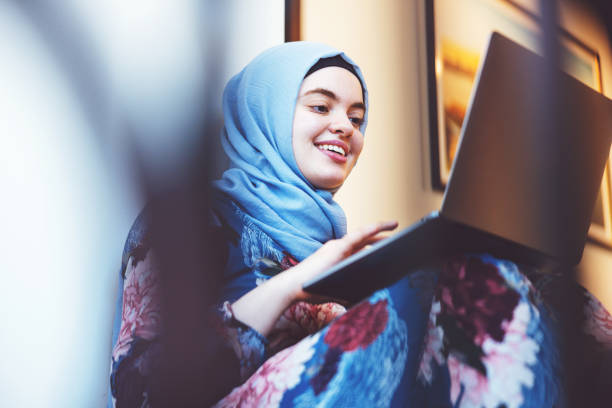 Young Middle Eastern Female Working from Home Middle Eastern Girl Casually Seated at the Stairway and working on her laptop middle eastern culture stock pictures, royalty-free photos & images