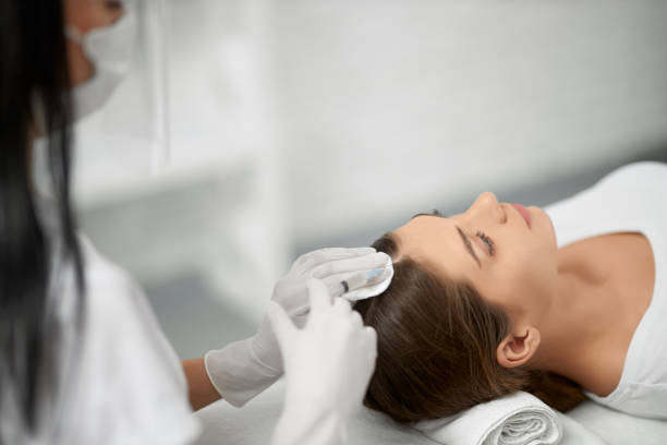 Beautician in protective mask doing procedure for hair. stock photo