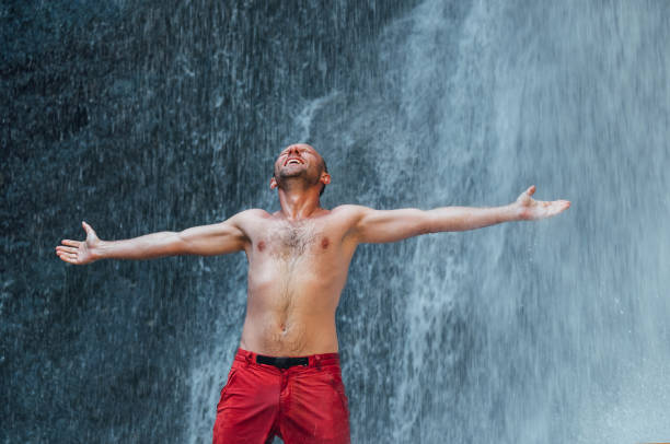 istock Middle-aged man dressed only in red trekking shorts standing under the mountain river waterfall spread arms and enjoying the splashing Nature power. Traveling, trekking and nature concept image. 1317678702