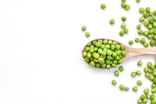 green peas on wooden spoon on white background.