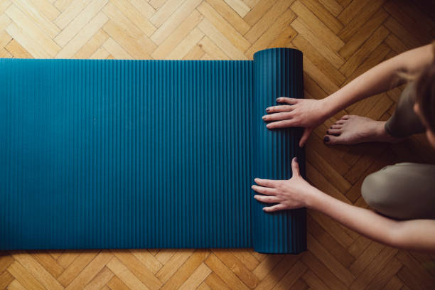 木製の床に青いエクササイズマットを折る女性の手のクローズアップ - エクササイズマット ストックフォトと画像