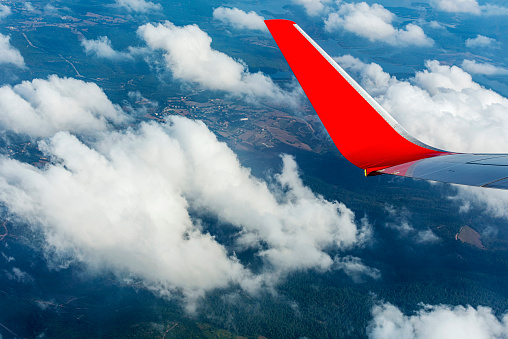 View through window of red airplane wing in cloudy sky.