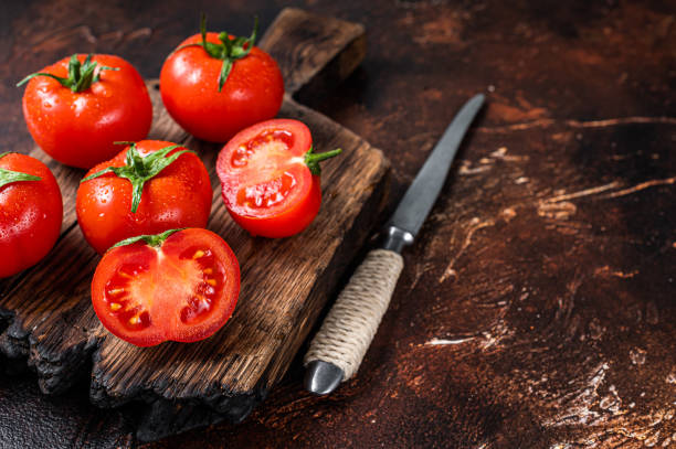 istock Cut Red cherry tomatoes on wooden cutting  board. Dark background. Top view. Copy space 1317692093