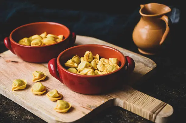 Fresh italian pasta Cappelletti in a red rustic bowl on a wooden cutting board on a dark rustic background. with copy space