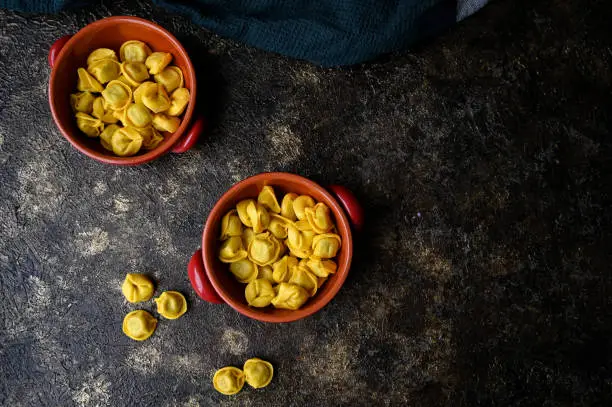 Fresh italian pasta Cappelletti in a red rustic bowl on a dark rustic background. Top view with copy space