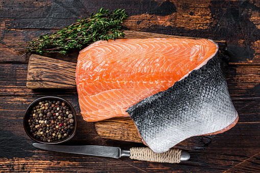 Salmon fillet fish on a  wooden board with herbs and salt. Dark wooden background. Top view.