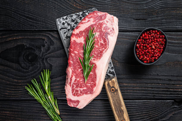 Fresh Raw new york strip beef steak on a butcher meat cleaver. Black wooden background. Top view Fresh Raw new york strip beef steak on a butcher meat cleaver. Black wooden background. Top view. barbecue beef stock pictures, royalty-free photos & images