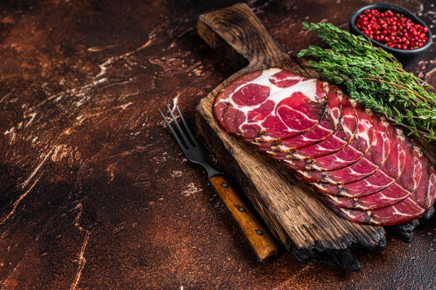 istock Sliced cured coppa ham  on wooden board with thyme. Dark background. Top view. Copy space 1317699678