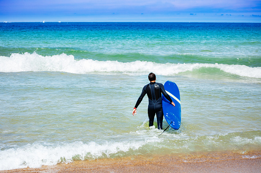 Portrait from the back of the man walking with surfboard in wetsuit to the sea waves