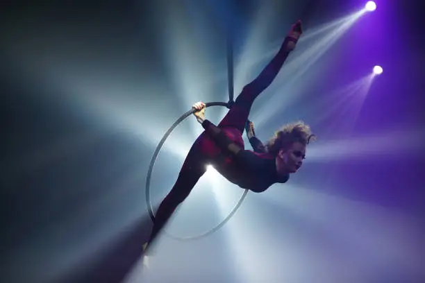 Young woman performing acrobatic element on aerial ring indoors, air stretch, splits in air