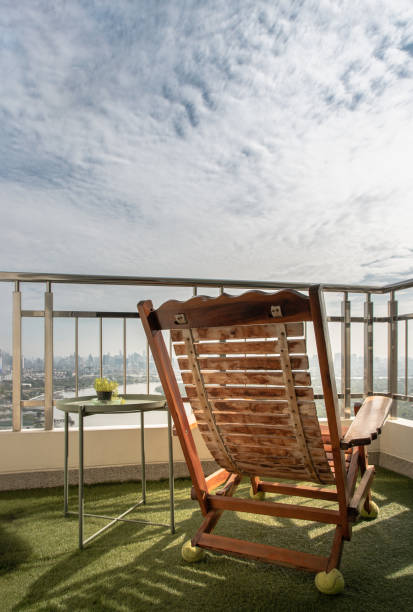 istock A wooden reclining chair with small tree on side table with Stainless steel balcony railing overlooking city view. 1317712596