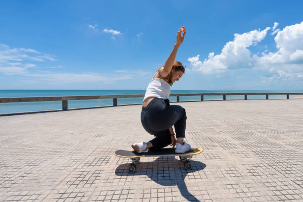 jóvenes asiáticas montando surfskate tabla. deporte al aire libre de moda en tailandia, asia. - patinaje en tabla larga fotografías e imágenes de stock