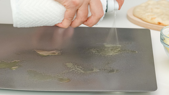 Woman using olive oil spray on baking pan. Pizza step by step baking process, recipe