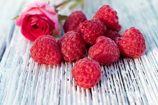 Raspberries and blurred pink rose on a white wooden background. Summer concept and concept of vitamin berries. Selective focus with shallow depth of field.