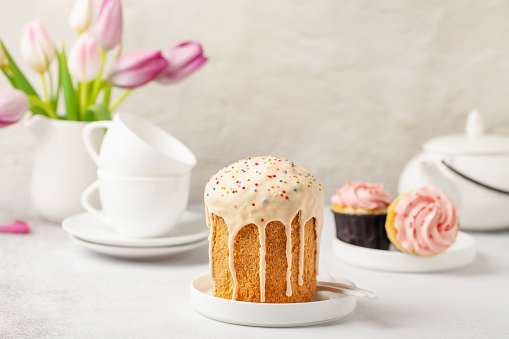 Easter cakes Kulich, tulips and white utensils for a tea ceremony on a bright background. Holiday concept