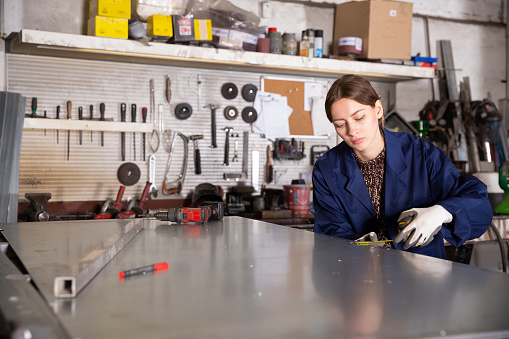 Young woman  worker working with metal sheet and using measuring tape  in workshop
