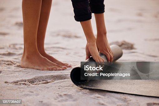 istock Cropped shot of an unrecognizable woman rolling up her mat after a yoga session on the beach at sunset 1317735407