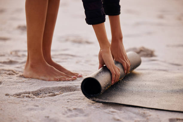 Cropped shot of an unrecognizable woman rolling up her mat after a yoga session on the beach at sunset The beach is the best place for yoga exercise mat stock pictures, royalty-free photos & images