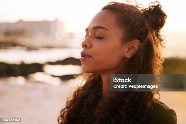 Foto De Una Atractiva Joven Sentada Sola En Una Colchoneta Y Meditando En La Playa Al Atardecer Foto de stock y más banco de imágenes de Relajación