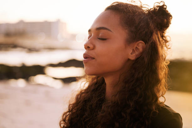 strzał atrakcyjnej młodej kobiety siedzącej samotnie na macie i medytującej na plaży o zachodzie słońca - nature wellbeing freshness healthy lifestyle zdjęcia i obrazy z banku zdjęć