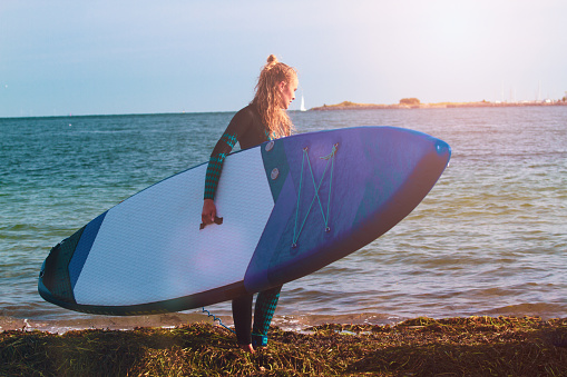 Fit danish female with long, blonde hair SUP paddle-boarding in the sea around Svanemøllen Beach in Copenhagen, Denmark