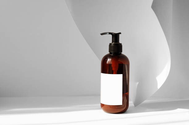 istock Brown bottle with dispenser for cream, shampoos, oils with blank label on white background with an unfolded sheet of paper. Solid background with copyspace and falling shadow from window 1317739437