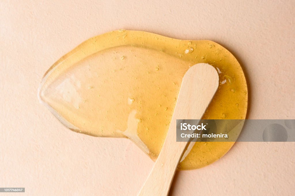Liquid sugar wax smear with spatula Liquid sugar wax smear with spatula on beige background Hair Removal Stock Photo