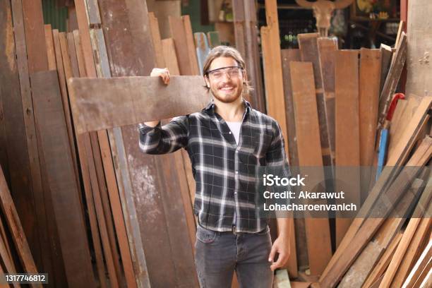 Young Caucasian Carpenter Man Is Carrying Plank Of Wood In His Own Garage Style Workshop For Hobby Stock Photo - Download Image Now