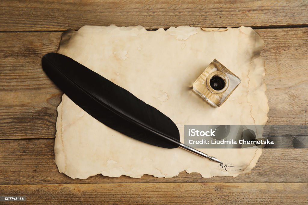 Feather pen, inkwell and parchment on wooden table, top view Ink Well Stock Photo