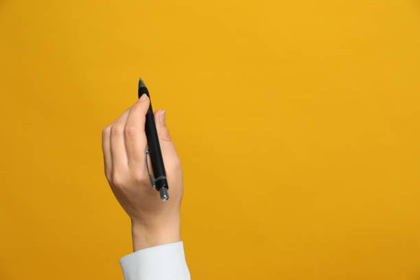 donna mancina che tiene la penna su sfondo giallo, primo piano. spazio per il testo - left handed foto e immagini stock