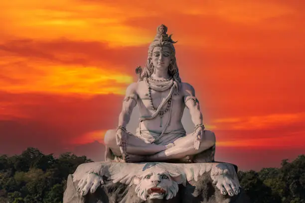 Statue of meditating Hindu god Shiva against the red sky on the Ganges River at Rishikesh village in India, close up