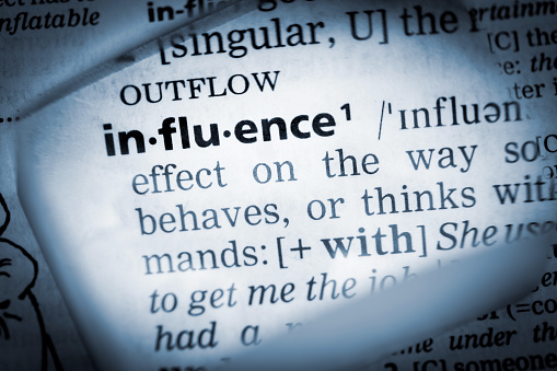 The Dictionary definition of the word “influence” photo taken through magnifying glass from a page of a dictionary with selective focus.