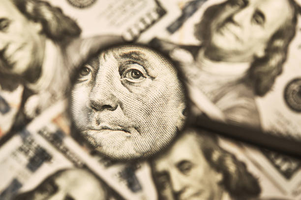 istock Magnifying glass on a pile of 100 dollar banknotes 1317757671