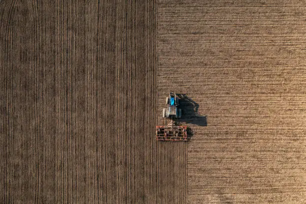 Top view of a tractor harrowing soil on an agriculture field. Agricultural tillage or land preparation.