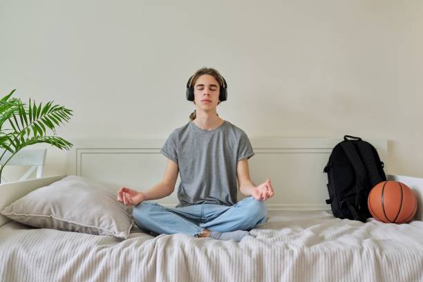 瞑想をリラックスベッドの上に蓮の位置に座っている男性ティーンエイジャー - lotus position audio ストックフォトと画像