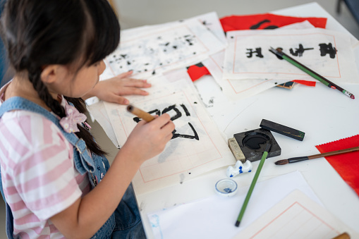 Joyful little Asian girls practice Chinese calligraphy at living room.