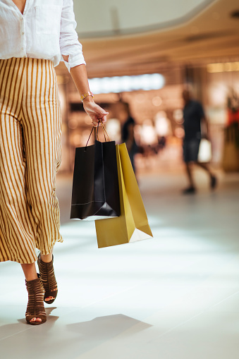 Unrecognisable woman walking through the shopping mall while holding paper shopping bags