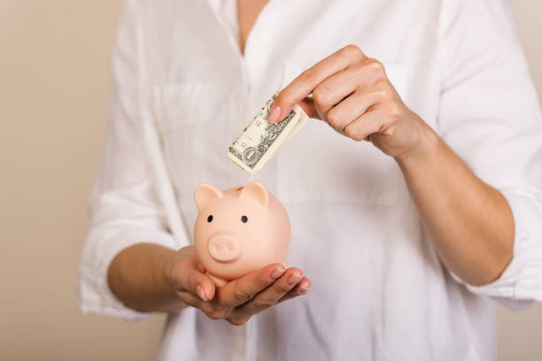 istock Woman putting dollar bancnote into piggy bank on light blue background, closeup. Space for text 1317762885