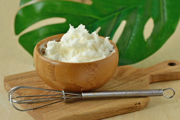 Face cream made of shea butter and argan oil in wooden bowl with whisk on small chopping board stock photo