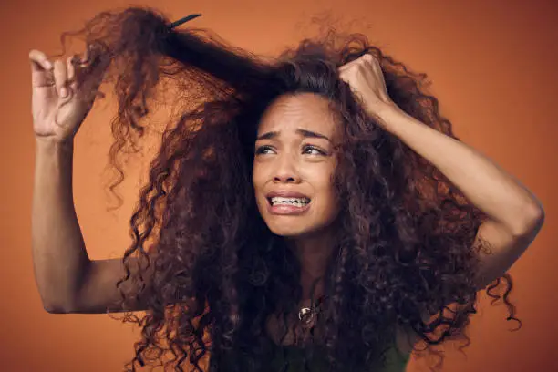 Photo of Shot of a woman crying while combing our her curls against an orange background