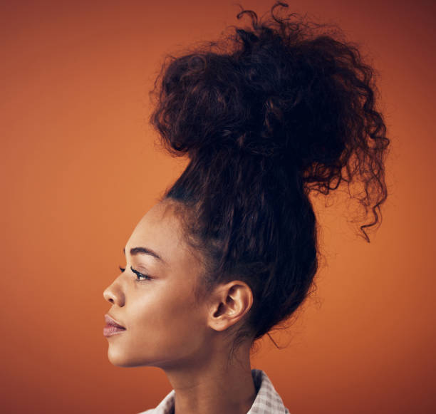 Shot of a young woman wearing her hair in a bun against an orange background The bigger the bun, the bigger the dreams black woman hair bun stock pictures, royalty-free photos & images