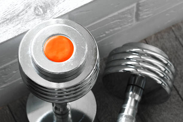 Metal heavy dumbbells on the floor with orange tag for text Dumbbells on the floor near a brick wall, sports metal weight training equipment for muscle development, healthy lifestyle hantel stock pictures, royalty-free photos & images