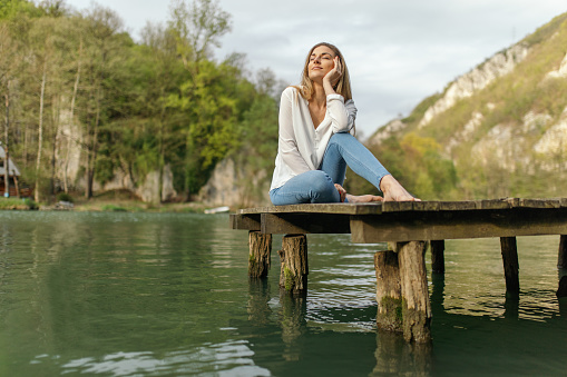 Young beautiful woman sitting and relaxing on the dock far away from the city. She is enjoying her view and some fresh air.