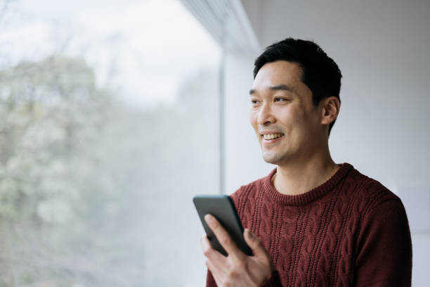 Smiling East Asian man using smart phone at home