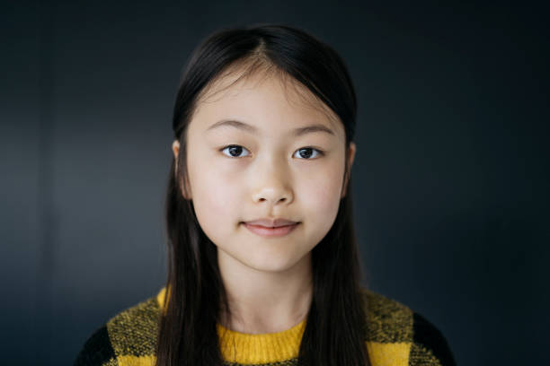 Headshot of Chinese teenage girl in casual clothing Close-up of 13 year old girl with long black hair wearing yellow and black pullover sweater and looking at camera with contented expression. london girl stock pictures, royalty-free photos & images